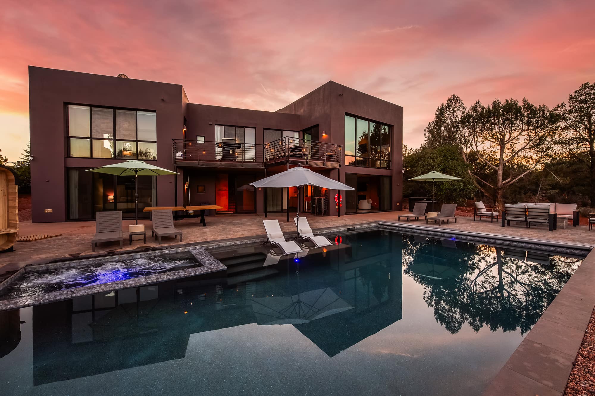 The pool at dusk, loungers and red rocks under a pink sky